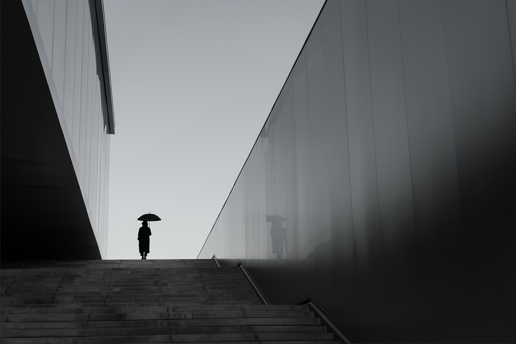 Person standing at the top of stairs holding an umbrella between modern buildings - Used on Capco Insurance