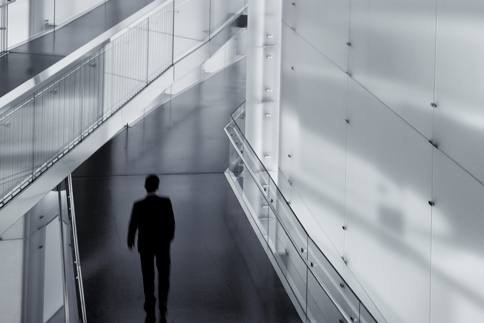 Professional walking through a modern office corridor with glass walls and railings - Used on Capco Policies