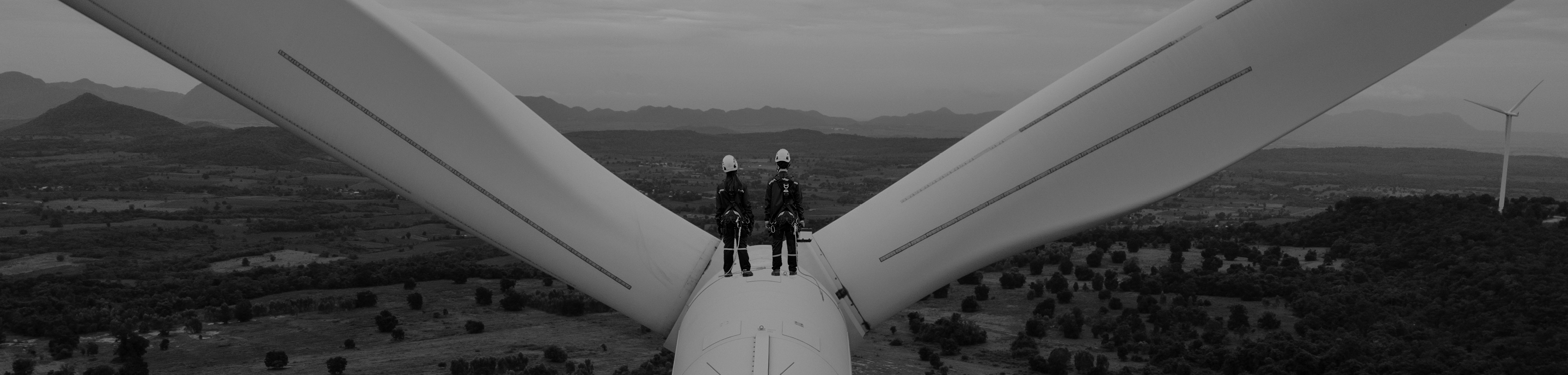 Two technicians standing atop a wind turbine overlooking a landscape with additional turbines.