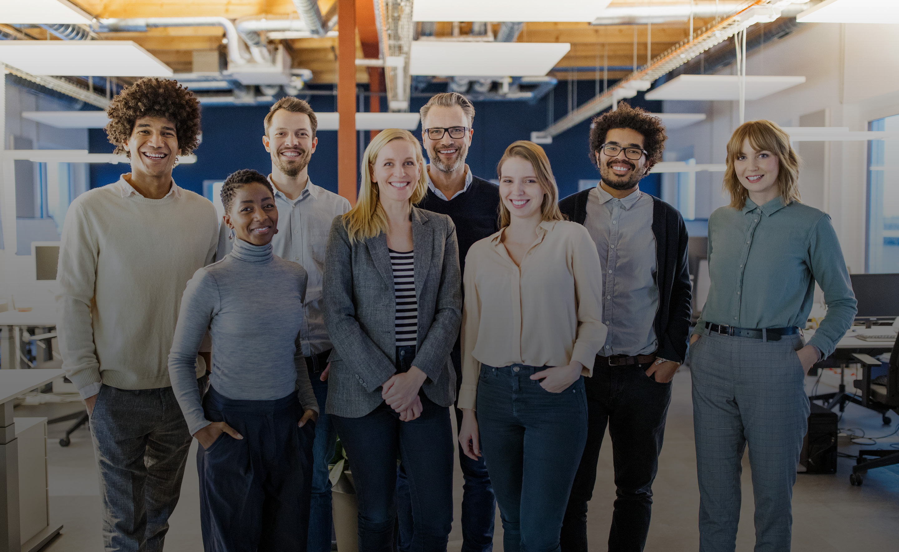 Group of eight people standing in an office facing forward and smiling. 